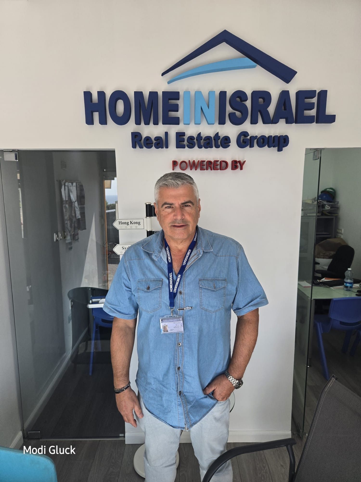 מודי גליק במשרדי Home in Israel בנתניה, מול שלט הסוכנות